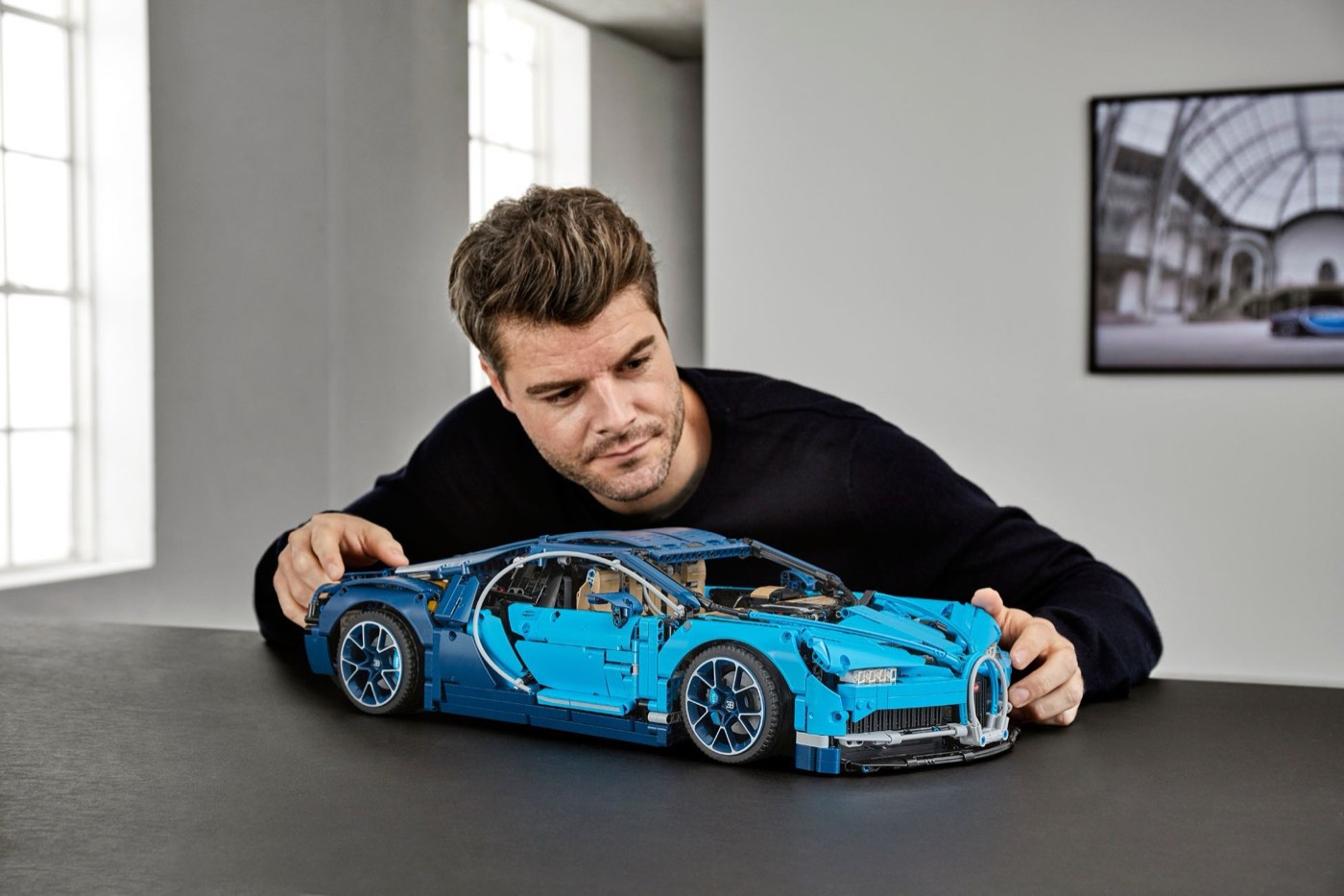 Builder leaning over the completed LEGO Technic Bugatti Chiron 42083 in blue on a dark table, showing the full length of the model