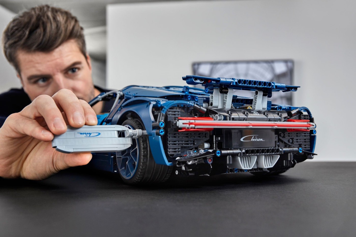 Hand holding the printed Chiron nameplate element at the rear of the LEGO Technic Bugatti Chiron 42083, with the rear wing raised