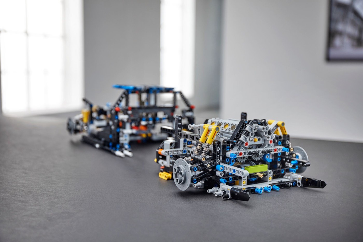 Two LEGO Technic Bugatti Chiron 42083 subassemblies on a table, the chassis behind and the gearbox and suspension module in front